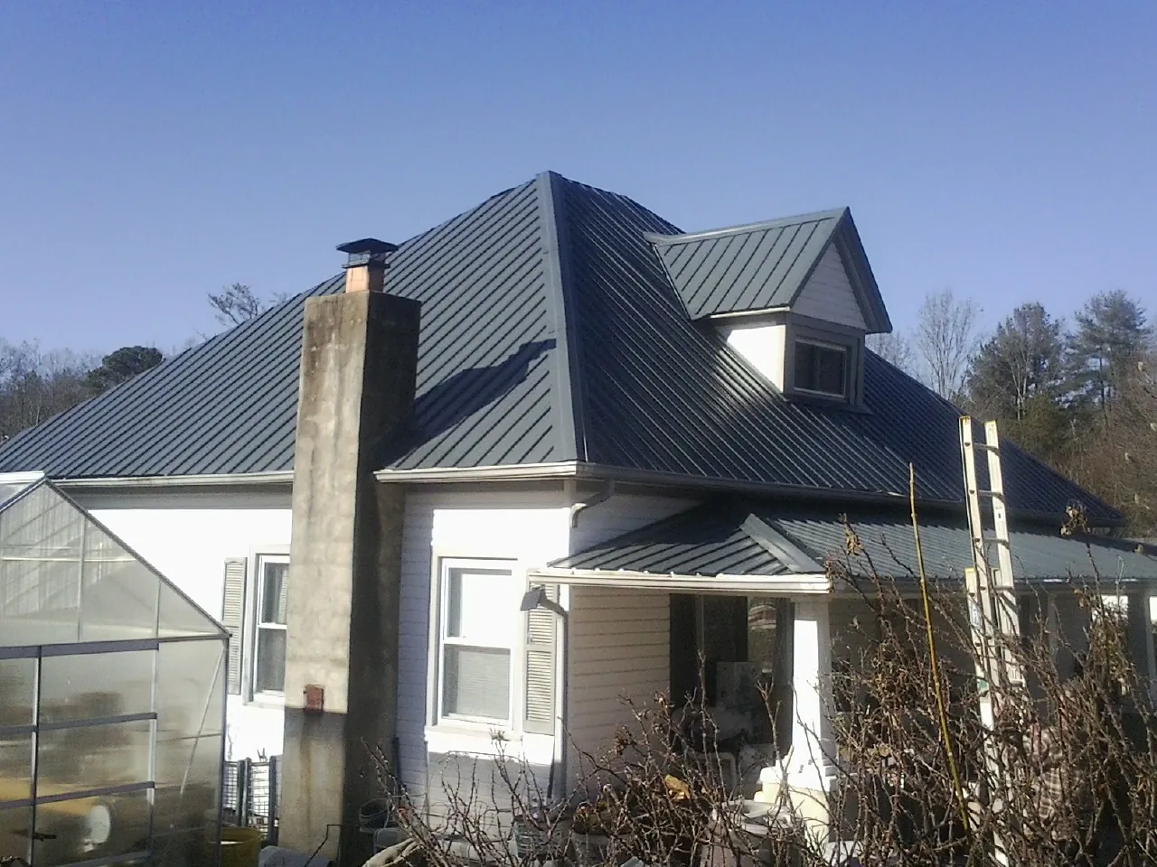 Dark blue standing seam metal roof on a white farmhouse with dormer — Slate & Tile Roof Repair by Roofing Brothers in Neihart