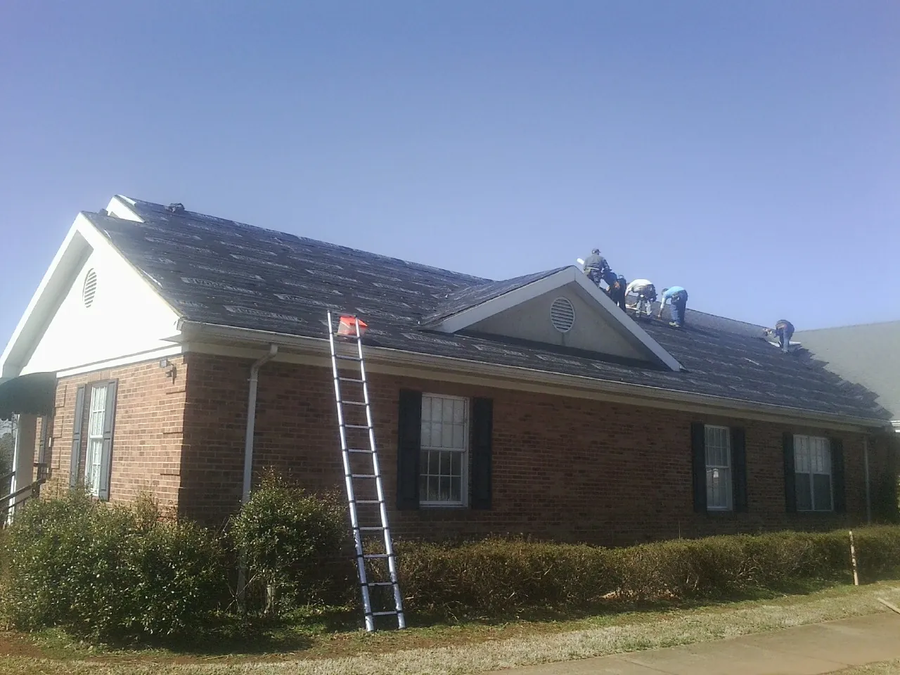 Crew tearing shingles off a brick ranch roof with a ladder set — Metal Roof Repair work by our crew in Neihart
