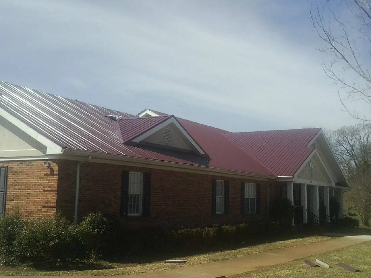 Red metal roof with gabled entries on a long brick building, from a Hail Damage Roof Repair job in Neihart