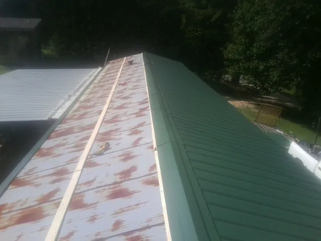 Old rusted panels beside newly installed green metal roofing — Wind Damage Roof Repair by Roofing Brothers in Neihart