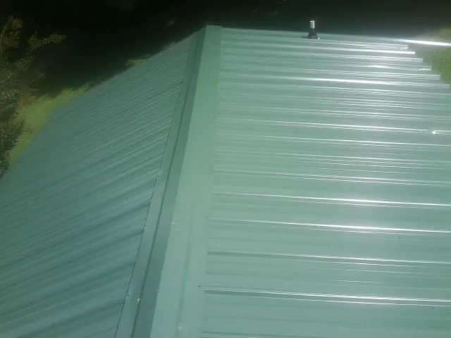 New green metal panels meeting at the ridge of a roof — Flat Roof Repair work by our crew in Neihart