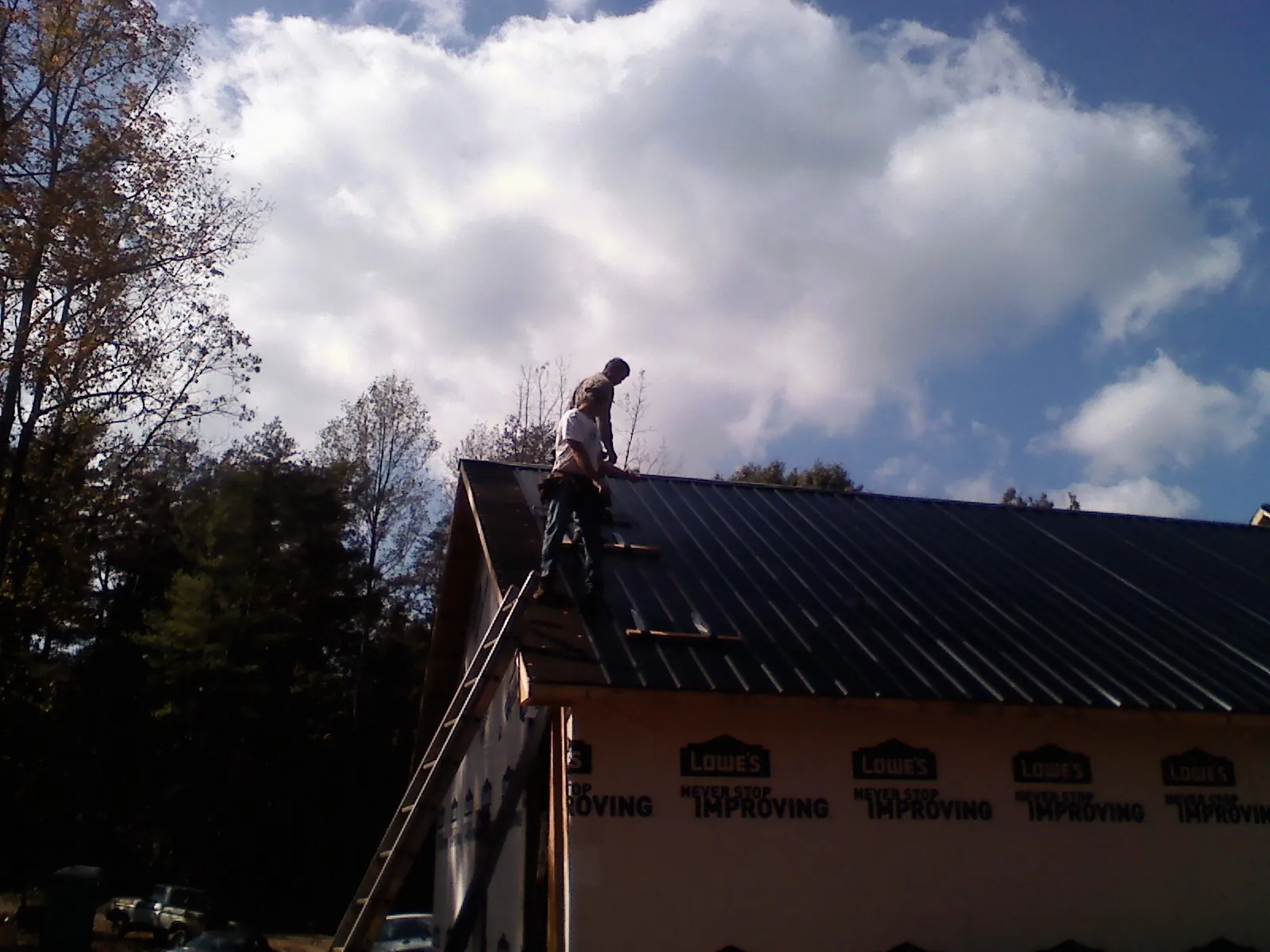 Roofer fastening dark metal panels high against a cloudy sky, from a Roof Inspection job in Neihart