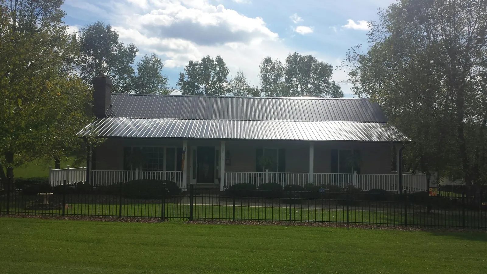 Gray metal roof on a brick ranch with a full width front porch — Gutter Guard Installation work by our crew in Neihart