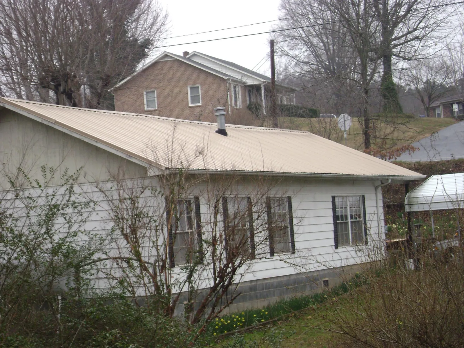 Tan metal roof on a white sided house set into a hillside — Commercial Roofing by Roofing Brothers in Neihart