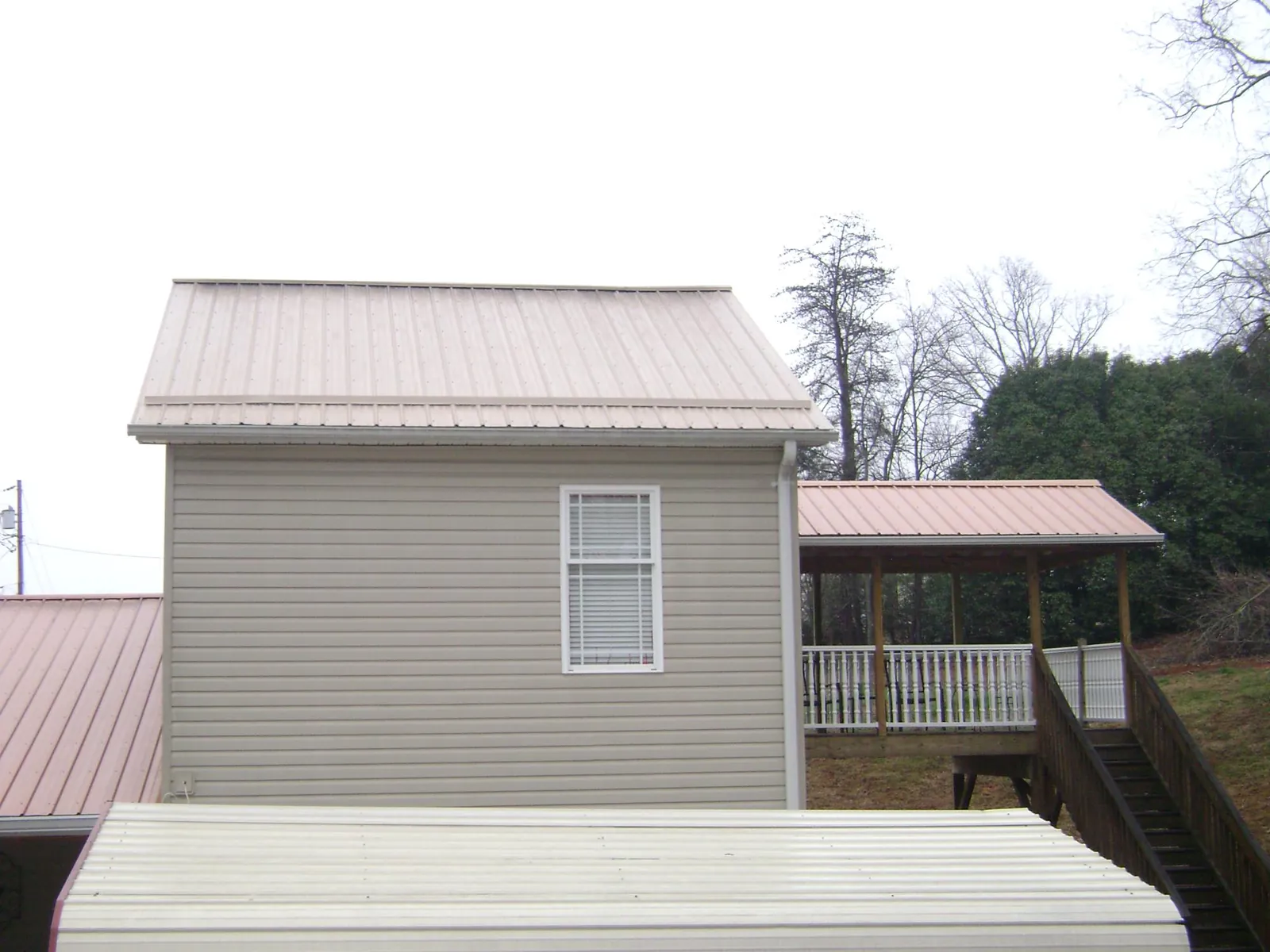 Tan metal roofs on a two story addition and attached porch, from a Roof Replacement job in Neihart